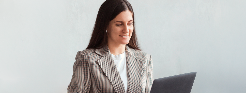 Mulher sorridente usando notebook, representando a rotina de uma gestora escolar que adota soluções de advocacia virtual para gerenciar documentos com eficiência.