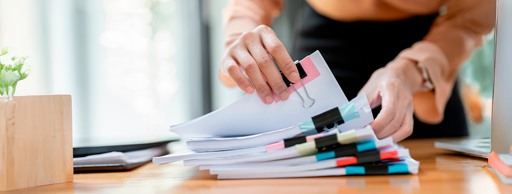 Pessoa organizando documentos administrativos sobre a mesa, simbolizando a transição de professores para funções de gestão escolar.